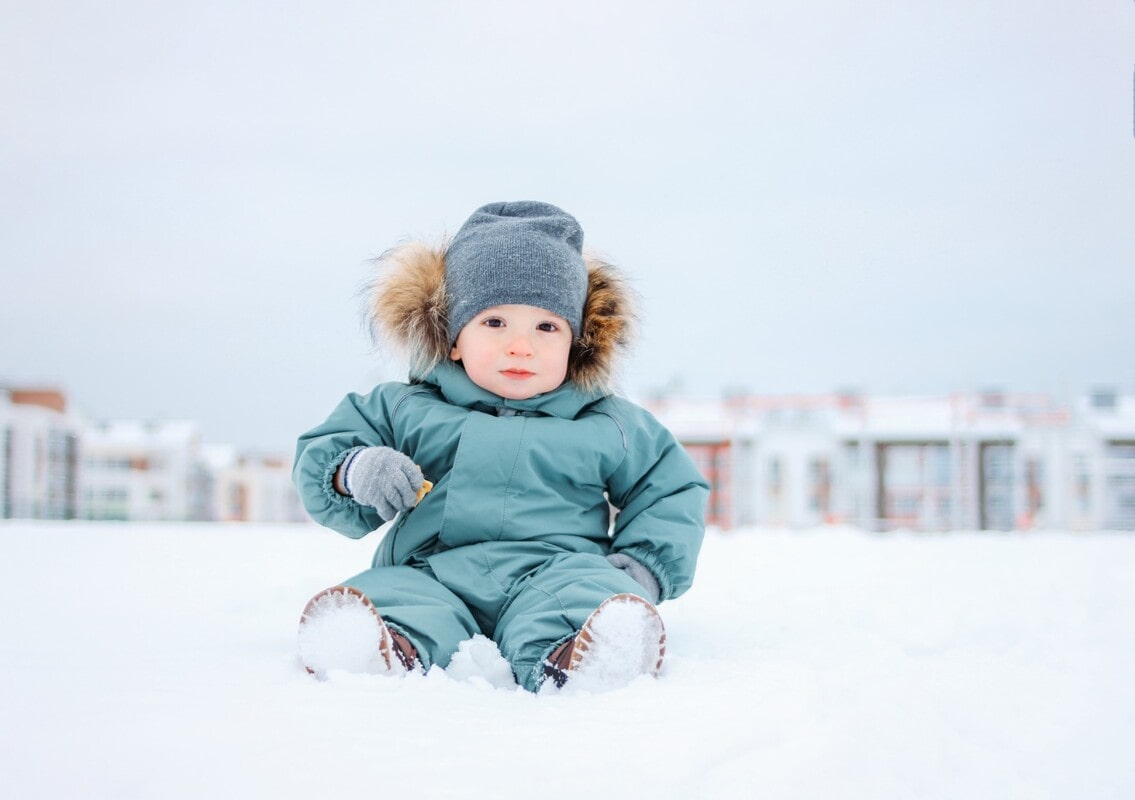 Dete u skafanderu sedi na snegu.