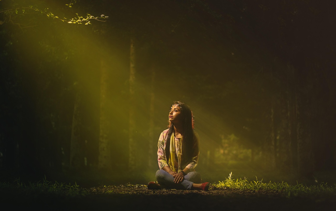 Žena sedi i meditira u šumi obasjana suncem 